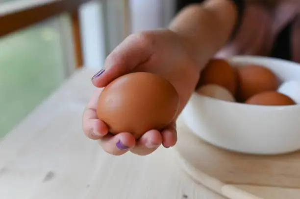 A fresh boiled brown egg with shell in the hand of a child on a breakfast table at home.
