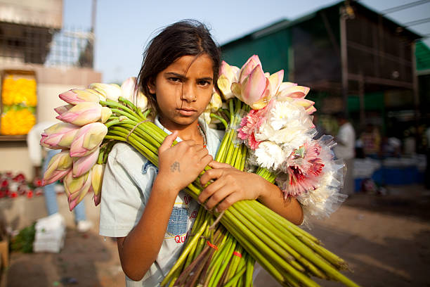 Young Indian flower vendor "Portrait of a young Indian flower seller taken at dawn.  Preety will sell flowers for her family from before sunup until mid day.  Other chores await her after that and then after a few hours of sleep, she will be at it again.  With luck, she will earn for her family the equivalent of one or two US Dollars, which will go a long way in providing for her family.   School is seldom an option for her." child labor stock pictures, royalty-free photos & images
