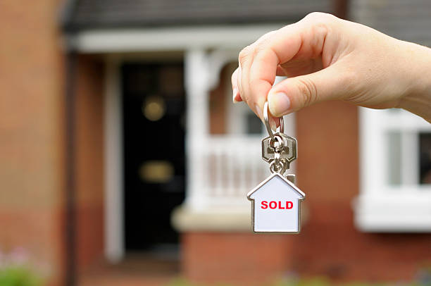 New homes New home concept portrayed by a female holding front door keys in front of a newly built house. keyring charm stock pictures, royalty-free photos & images