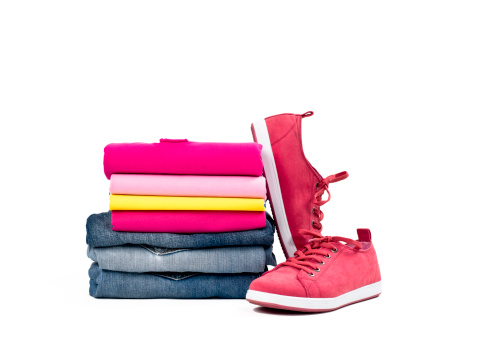 Multicolored casual clothes folded in pile with a pair of canvas shoes on white background