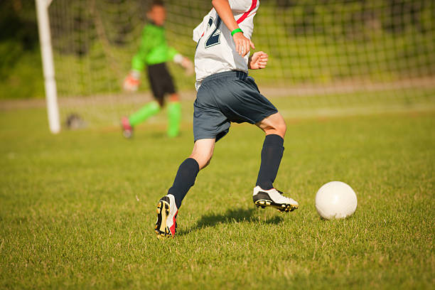 молодой мальчик фу�тболист приближением к цели с мячом - playing field kids soccer goalie soccer player стоковые фото и изображения