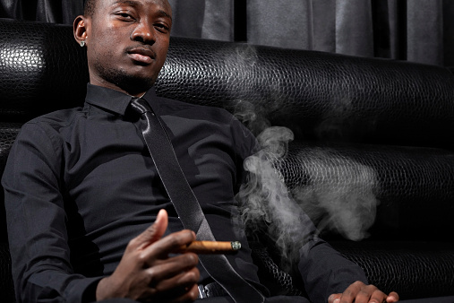 Side view of a mature businessman sitting in a limousine and smoking a Cuban cigar.   