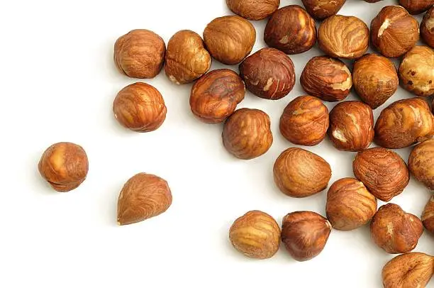 Shelled hazelnuts scatttered across a white background.
