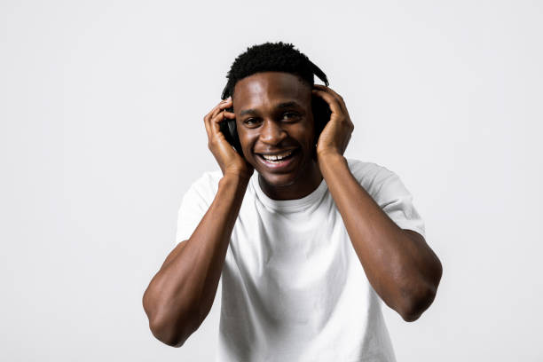 istock Handsome black african american guy over grey white background in studio isolated happy black guy model posing in t-shirt and headphones earphones opening mouth holding hands near face 1713009546