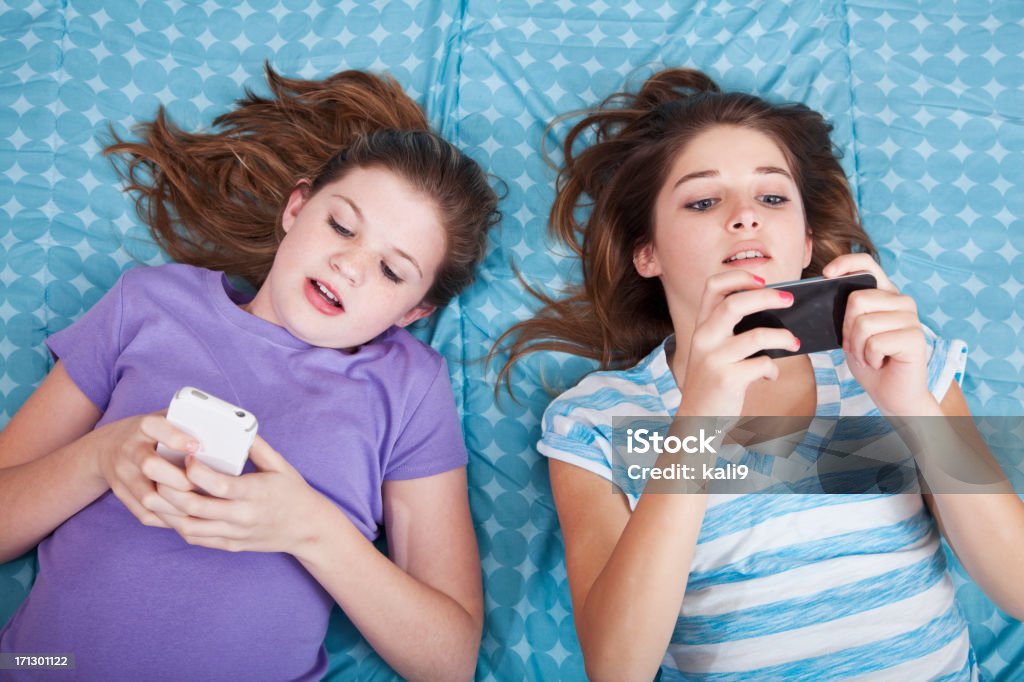 Girls texting "Preteen girls (12 years) lying on bed, texting on mobile phones." Pre-Adolescent Child Stock Photo