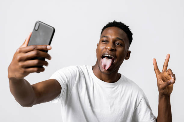istock African american model posing expressing different emotions at camera holding new modern laste serie phone smartphone in hands showing two fingers and opening mouth with tongue 1713011985