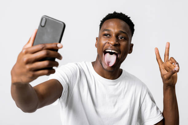 istock African american model posing expressing different emotions at camera holding new modern laste serie phone smartphone in hands showing two fingers and opening mouth with tongue 1713011999