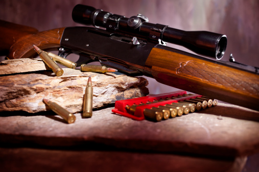 Rifle with sight and ammunition on rock shelf.  Selective focus on ammunition and edge of rifle.