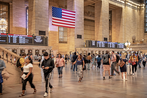 Grand Central, Manhattan, New York, USA - August 14th 2023:  People walking in the central hall beneath a large Stars and Stripes flag