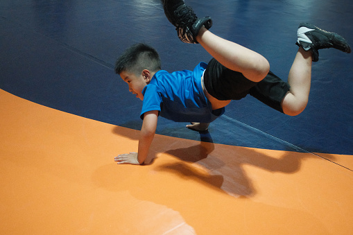 A young boy diligently warms up on a cushioned mat, gearing up for a wrestling practice session, displaying his dedication to the sport.