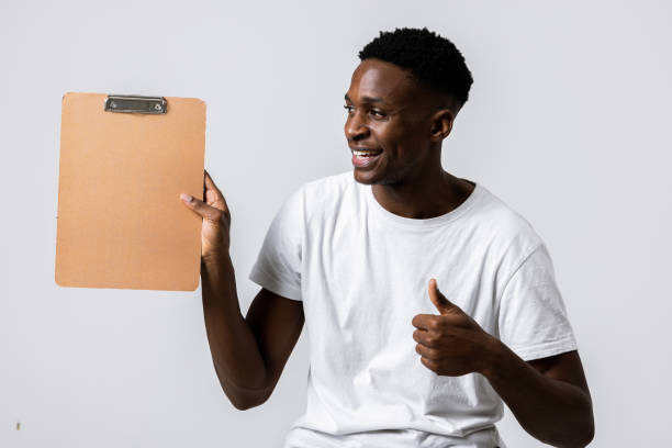 istock Happy attractive handsome cheerful african boy guy showitng thumb up holding empty folder showing at camera. Look there 1713015935
