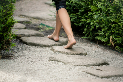 A woman walking down the stepping stones in a zen-like japanese garden.