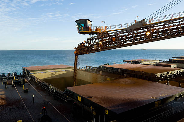 Cargo ship being loaded with crushed ore. A cargo ship being loaded with crushed ore from a mine site prior to export. mining conveyor belt stock pictures, royalty-free photos & images