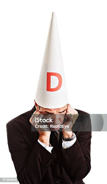 Businessman In Dunce Cap Looks Embarassed Grumpy And Resentful Stock Photo - Download Image Now