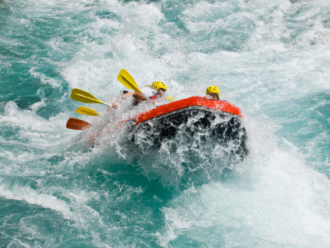 Group of people as they ride the rapids while white water rafting in the waves of a river