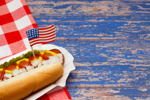 Ketchup, mustard, onion and relish on a hot dog with US Flag, focus on flag