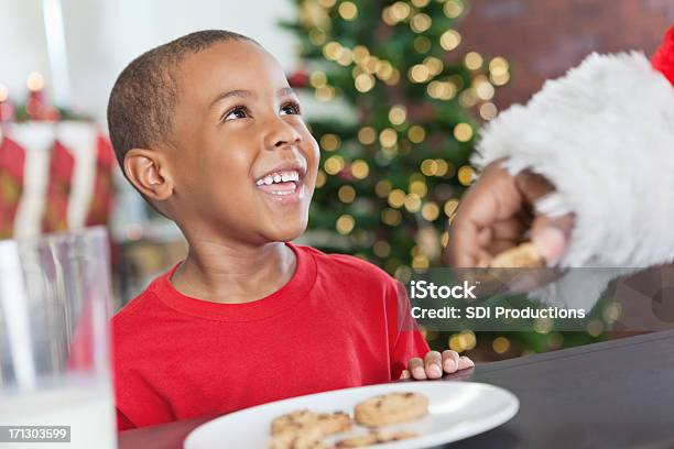 Poco Niño Sonriendo En Santa Comer Galletas De Navidad Foto de stock y más banco de imágenes de Navidad