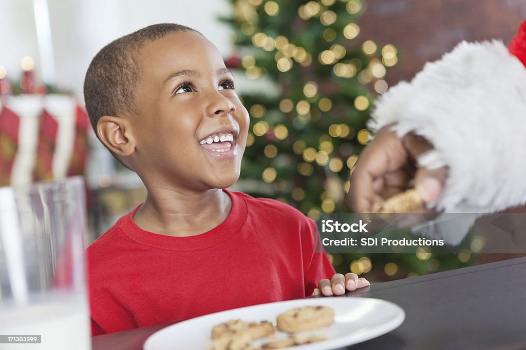 Ragazzino sorridente mangiare biscotti di Natale in Santa - Foto stock royalty-free di Natale