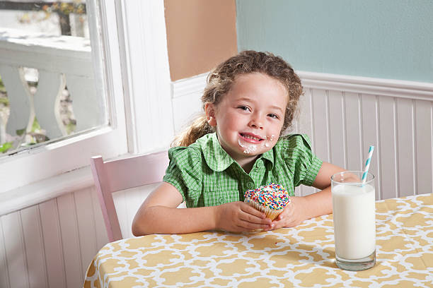 menina com um copo de leite comendo cupcake - sc0563 - fotografias e filmes do acervo