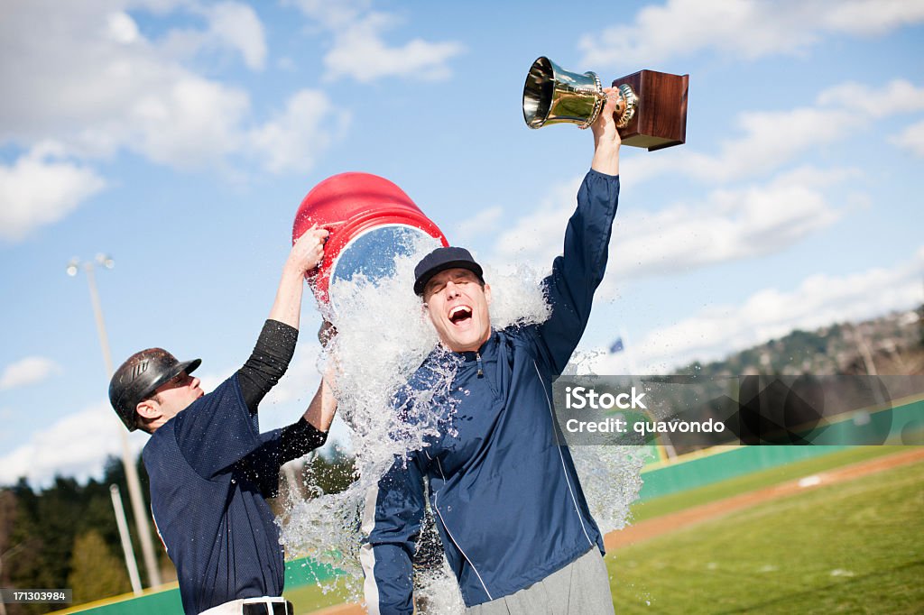 Player dumping Gatorade on coach holding a trophy Action sequence of baseball coach holding up a trophy celebrating and the players pouring water on him. Copy space. Winning Stock Photo