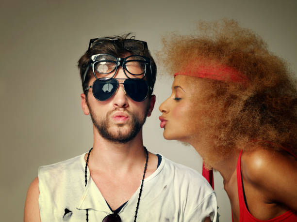 Young man wearing  many glasses while his girlfriend trying to kiss him