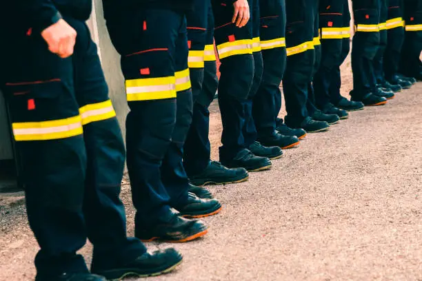 Many unrecognizable firefighters lined up in reflective pants.