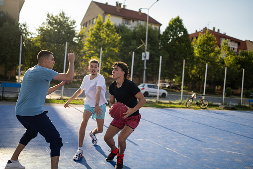 Group of people, male friends together playing basketball outdoors on basketball court.