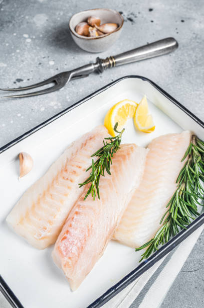 istock Uncooked Raw cod loin fillet steaks with herbs in kitchen tray. Gray background. Top view 1713046230