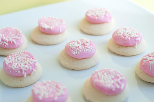 Pink Sugar cookies with white sprinkles on a plate. Focus is on center cookie.