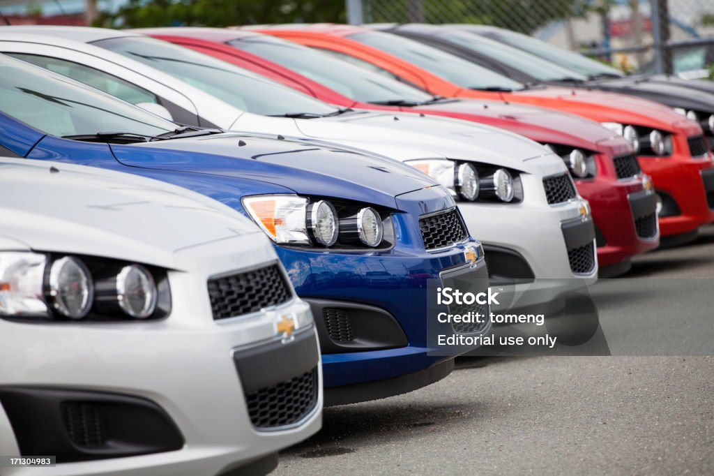 Chevrolet Sonic Vehicles in a Row "Halifax, Nova Scotia, Canada - July 2, 2012: New Chevrolet Sonic vehicles in a row at a car dealership.  Chain link fence is visible at end of row.  The Sonic replaced the Chevrolet Aveo in North America and was met with a much stronger market appeal.  The revised headlights, larger wheels, revised interior, and overall more aggressive design makes the Sonic a welcome replacement to the bland Aveo." Chevrolet Stock Photo