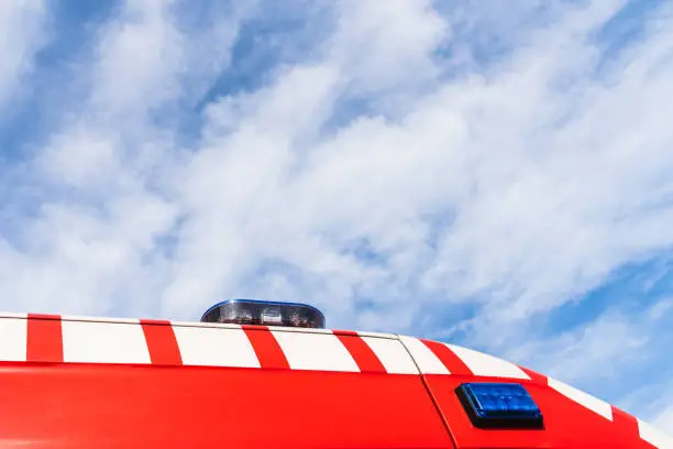Red roof of a medicalized ambulance over blue sky with clouds and copy space, to care for pandemic sufferers.