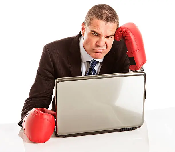 "This handsome businessman in boxing gloves and a laptop grimaces, frustrated and fed up - perhaps he's finding typing difficult! Isolated on white."