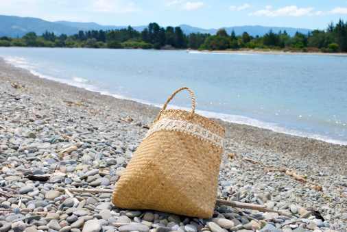 A traditional Maori kete on a coastal background. Kete is the Maori word for basket, they are woven from the dried leaves of the flax plant. Kete are used to collect Kai Moana (seafood) from the sea. 