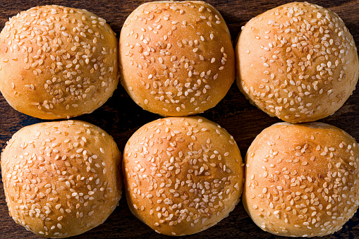 Burger bread buns in a row with sesame seeds on top, small size six bread hamburger bun flat lay top view