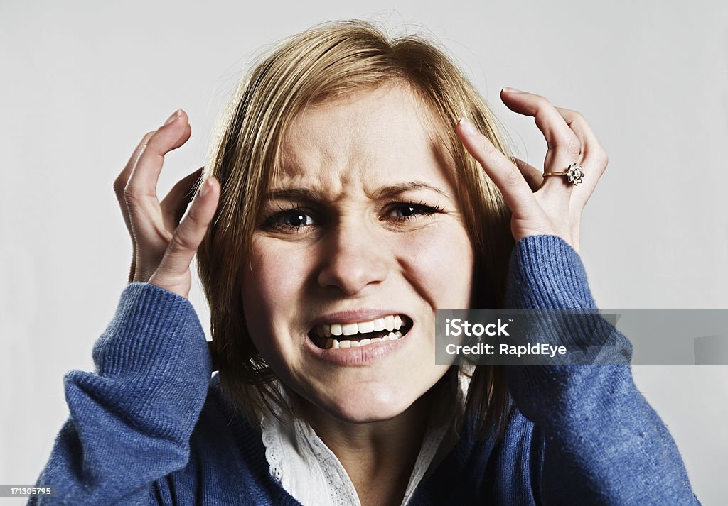 Young woman looks scared and frustrated "Emotional young blonde woman in blue, grimacing with her hands to her head. She could be scared, angry or in pain." 20-29 Years Stock Photo