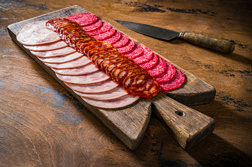 Cold cuts meat charcuterie slices in a row with pepperoni, chopped and sausage chorizo on a wooden cutting board on rustic table