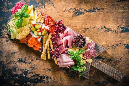 Mediterranean appeticer antipasto, on rustic wooden board with cold cuts meat charcuterie slices, manchego cheese, pepperoni, chopped, ham,  prosciutto and chorizo with bread sticks, crackers olives and pickles