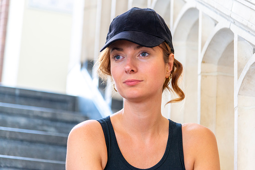 Portrait of a beautiful hipster woman with a black cap, situated on a staircase, looking away.