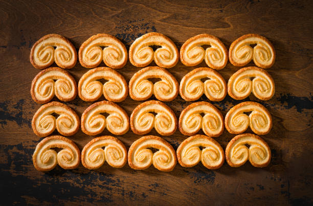 Palmiers, baked elephant ear puff pastry cookies in a row pattern on wooden background board table