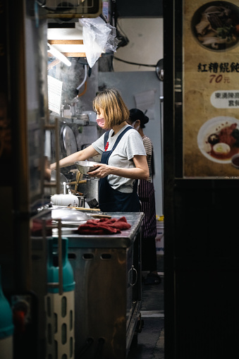 The dedicated proprietress of an authentic noodle shop can be seen fully immersed in the art of noodle preparation, ensuring that every dish is crafted with care and expertise.