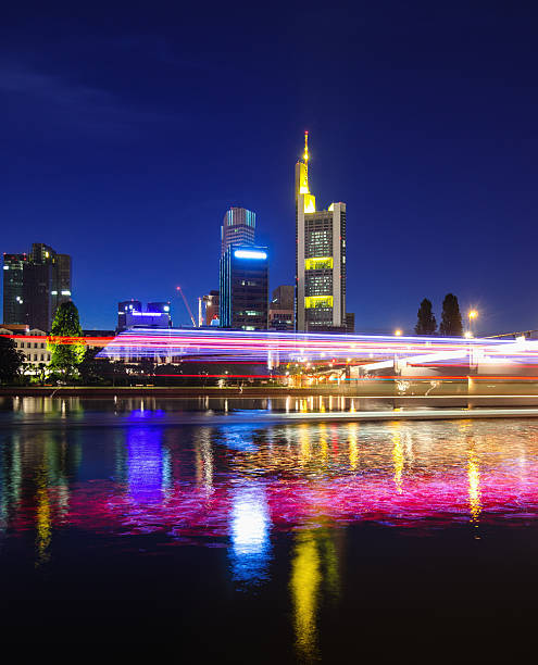 Light trails of a passenger ship on the river Main in front of the skyline of Frankfurt at dusk.