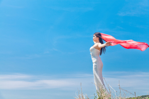 Portrait of pretty woman holding scarf in her hands standing on the hill under blue sky