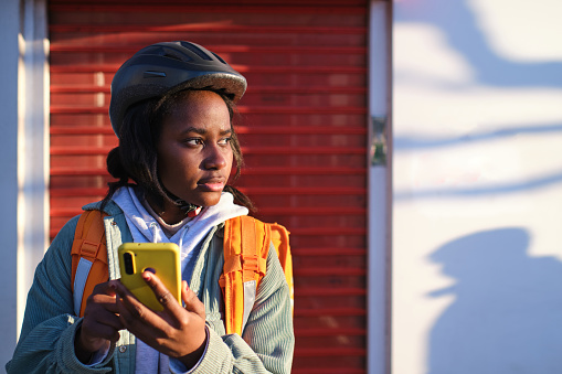 Front view of a food delivery African American woman using smart phone on street in city looking away with copy space
