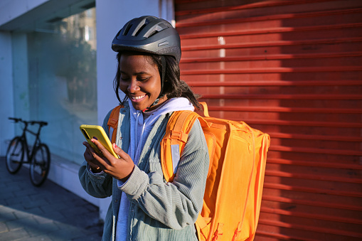 Portrait of a food delivery African American woman using smart phone in city.