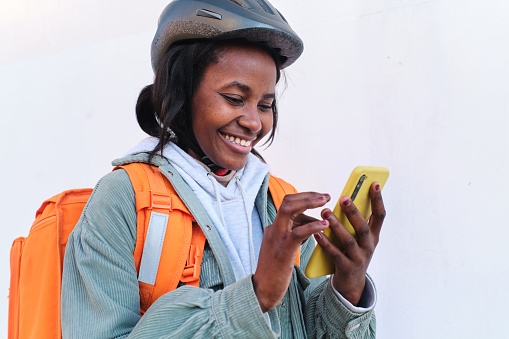 Portrait of a happy young delivery girl using her phone to notify her customer that her order is ready for delivery.