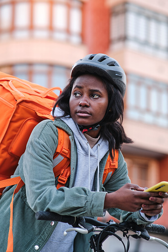 Vertical image of a food delivery woman on bike looking to cross the street.
