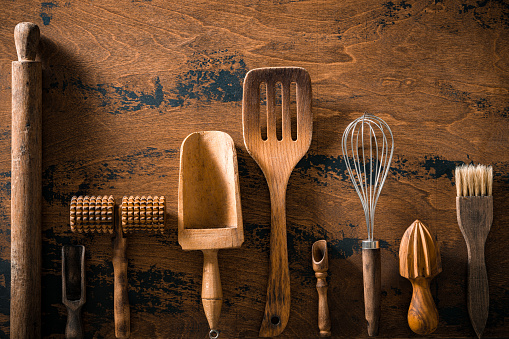 Wooden cutlery and kitchenware arrangement on rustic wood table board including rolling pin, ladles, whisk, juicer, knife and measure scoop spoon.