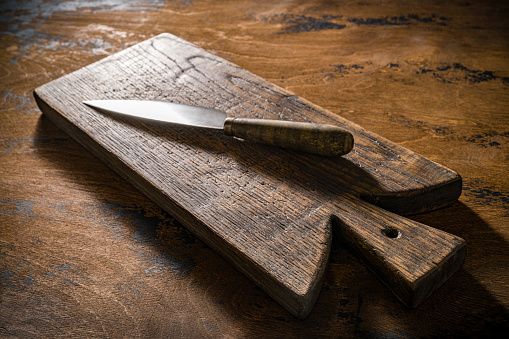 Wooden cutting board or chopping board and kitchen knife on rustic wood table low key kitchenware