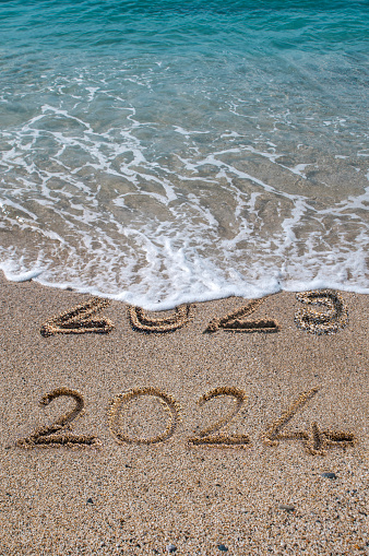 New year 2024 written on sandy beach with waves