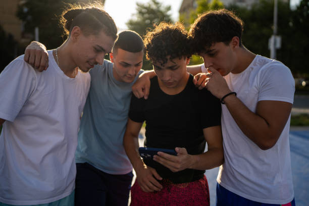 Group of people, male friends playing a game on smart phone together outdoors on basketball court.